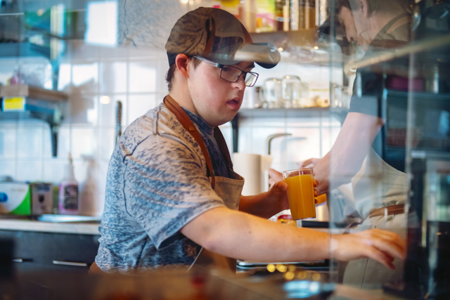 Man with down syndrome working at local coffee shop and making a drink.