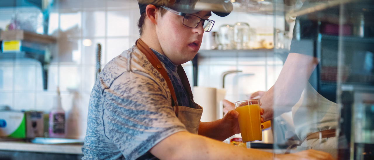 Man with down syndrome working at local coffee shop and making a drink.