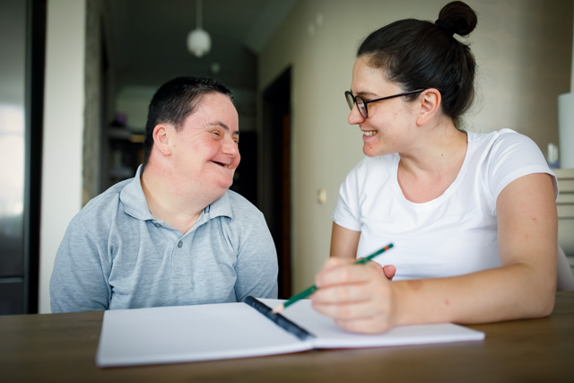 Young man with down syndrome and a woman sitting at a table, talking and taking notes together.