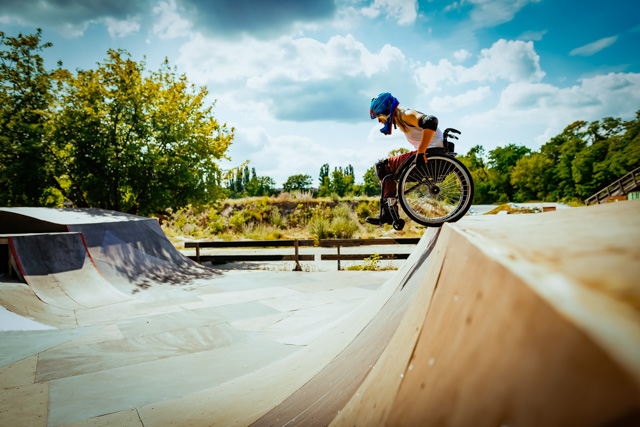 Young woman in wheel chair and wearing a helmet performing stunts in skate park.