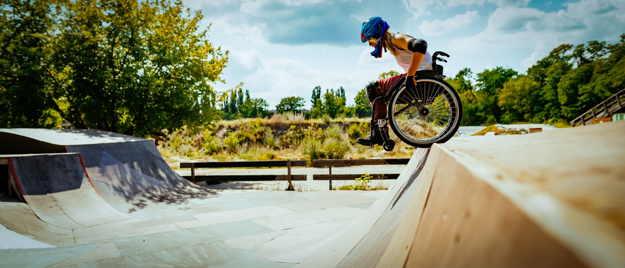 Young woman in wheel chair and wearing a helmet performing stunts in skate park.