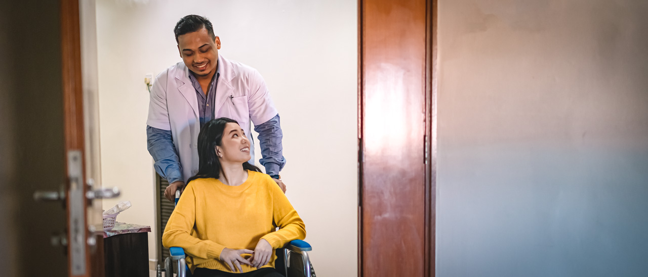 Male nurse talking to  a woman while pushing her wheelchair into a hospital room.