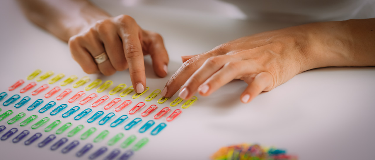 A close up of a pair of hands arranging paperclips in a rows based on colour.