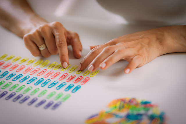 A close up of a pair of hands arranging paperclips in a rows based on colour.