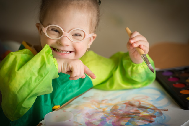 Girl with down syndrome making art and smiling.