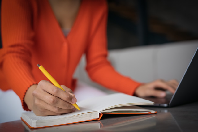 Closeup woman hand taking notes using laptop computer working online from home.
