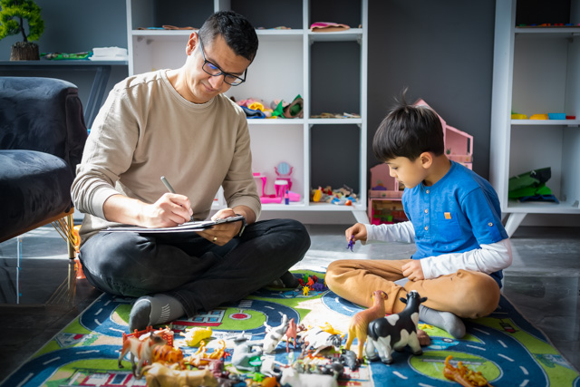 A child psychologist taking notes while observing a boy playing with toys.