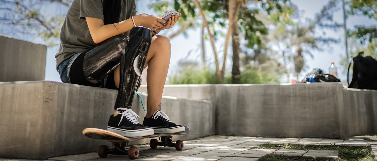 Disabled skateboarder woman sitting at a skate park and using a mobile phone.