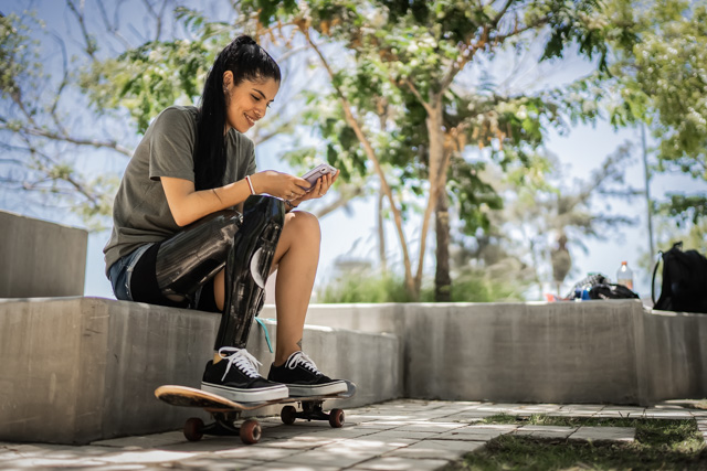 Disabled skateboarder woman sitting at a skate park and using a mobile phone.