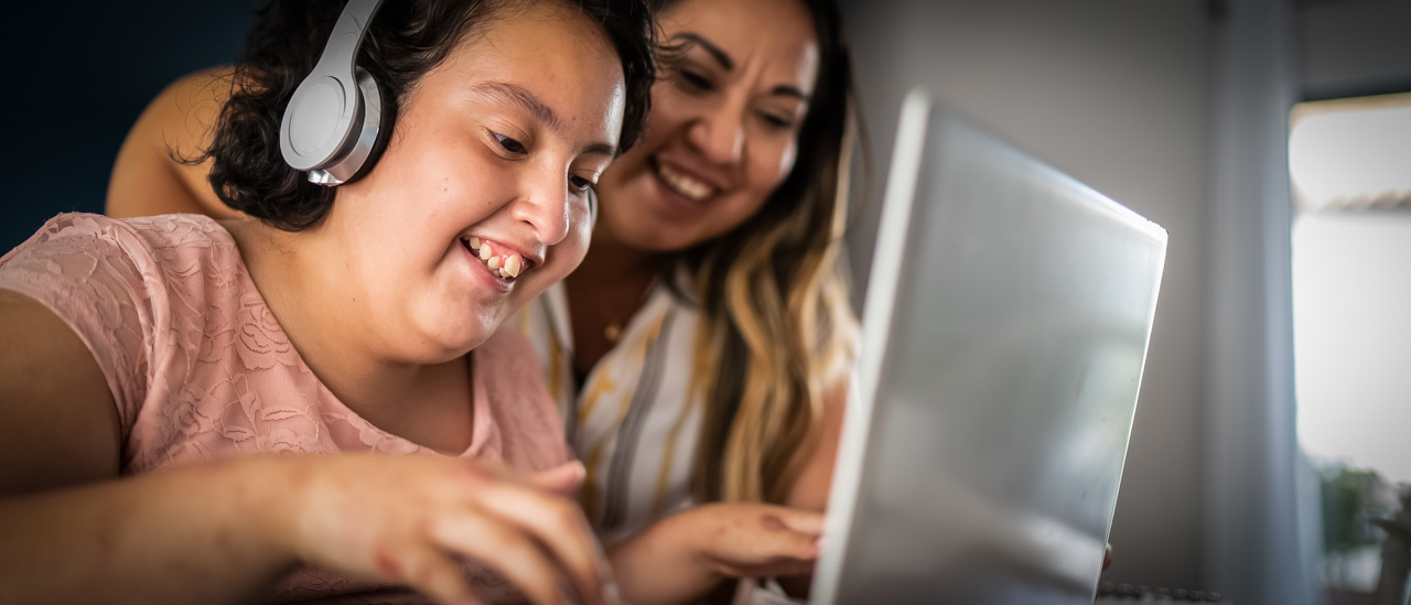 Mother showing her daughter, with psychomotor Intellectual disability, on how to use a laptop.