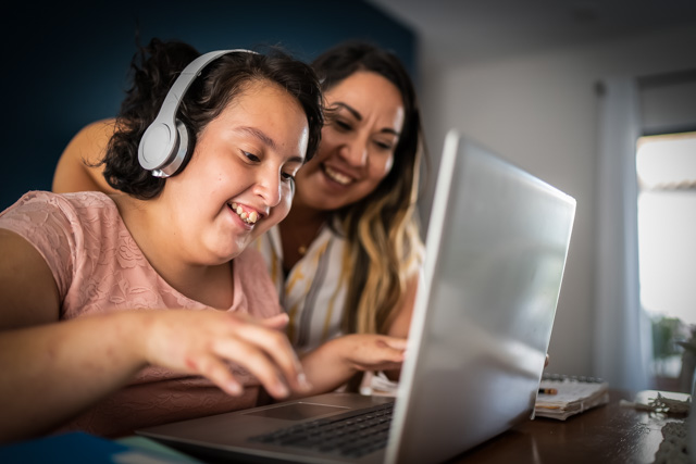 Mother showing her daughter, with psychomotor Intellectual disability, on how to use a laptop.