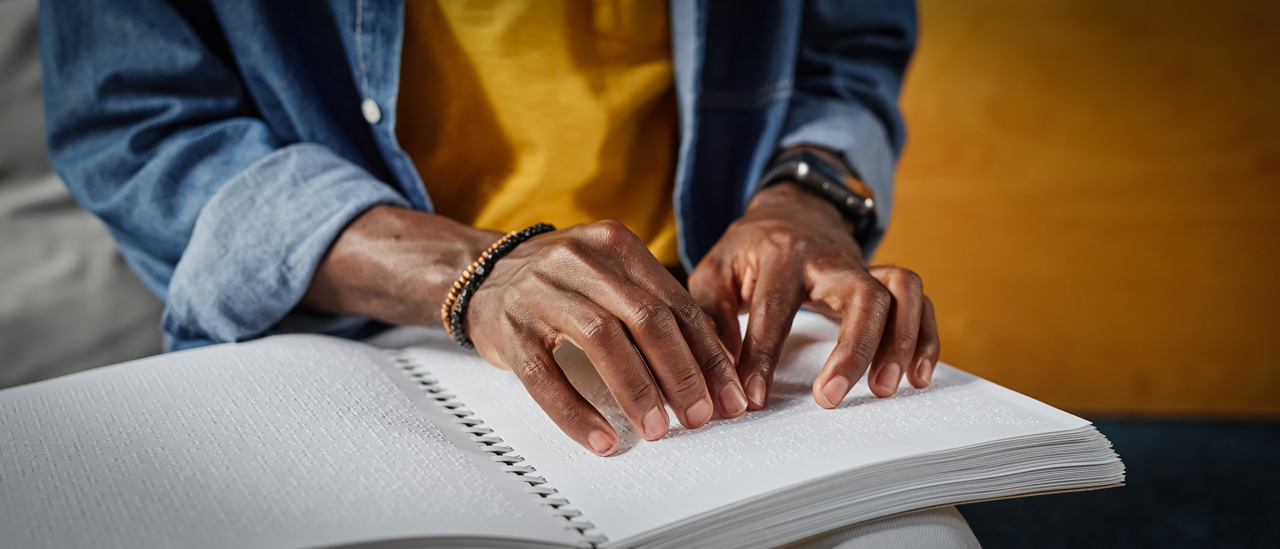 Close up of hands reading a book in braille.
