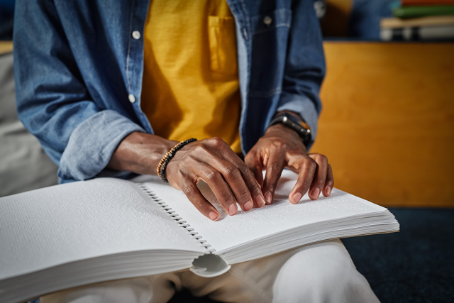 Close up of hands reading a book in braille.