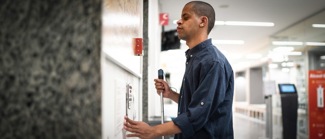 Visually impaired man reading braille on a wall while waiting for an elevator.