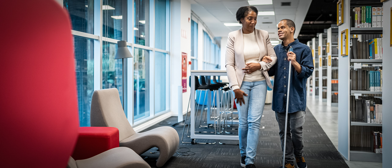 Teacher accompanying visually impaired at university library.