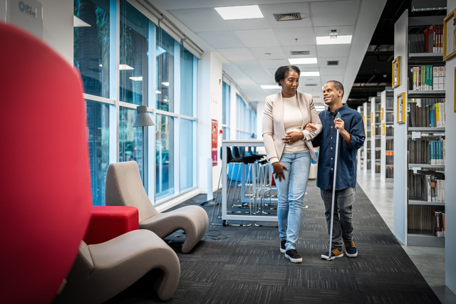 Teacher accompanying visually impaired at university library.