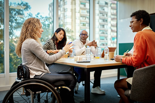 Woman in wheelchair having discussion with corporate team around a conference table.