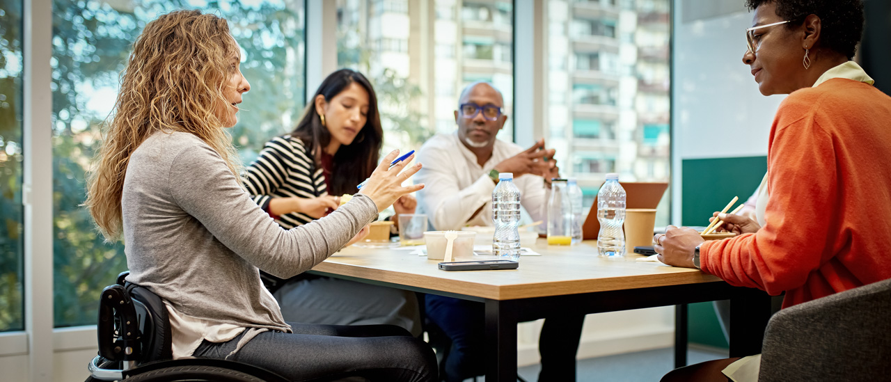 Woman in wheelchair having discussion with corporate team  around a conference table.