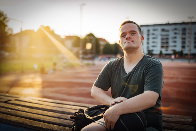 Portrait of a man with down syndrome sitting in the stands of a basketball court and confidently looking directly at the camera