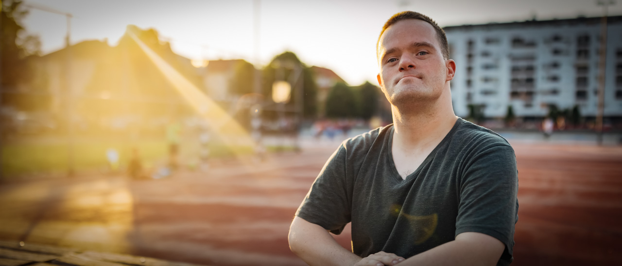 Portrait of a man with down syndrome sitting in the stands of a basketball court and confidently looking directly at the camera