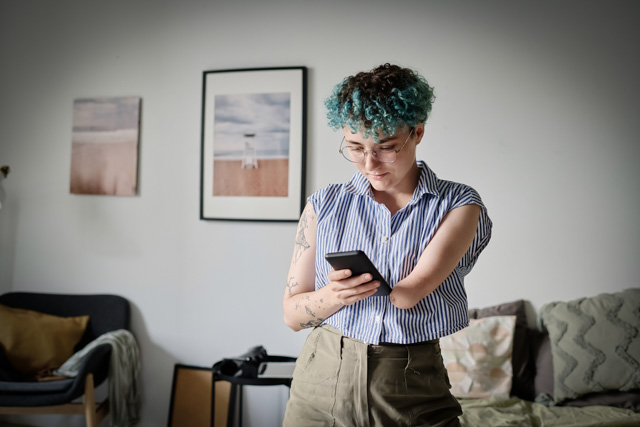 Woman with amputated arm reading message on her smartphone while standing in the living room.