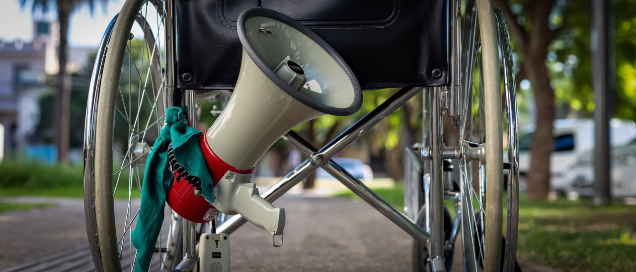 A disabled person's wheel chair with a megaphone hanging off the back of it.
