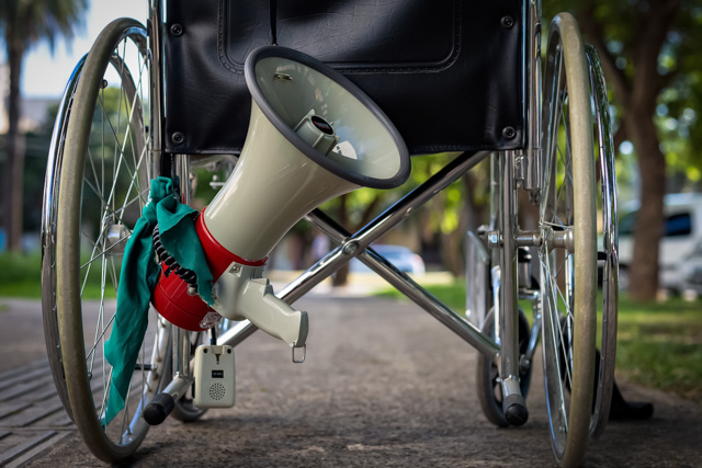 A disabled person's wheel chair with a megaphone hanging off the back of it.