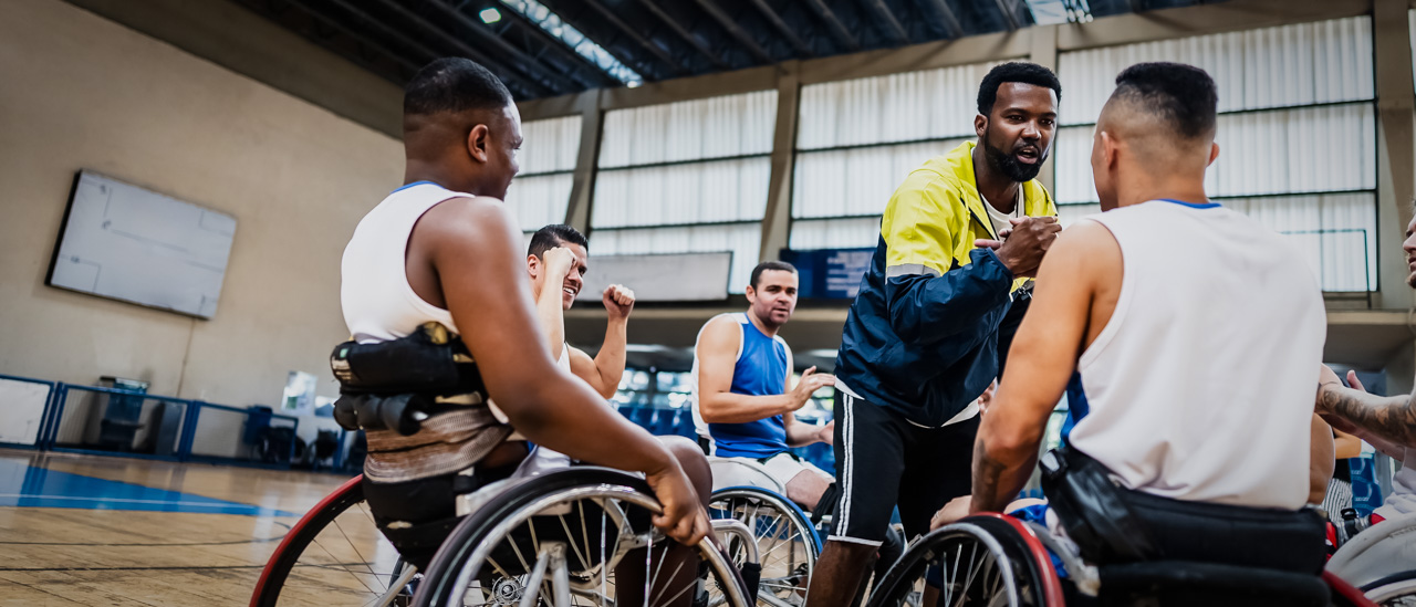 Coach handshaking wheelchair basketball player with his teammates showing support.