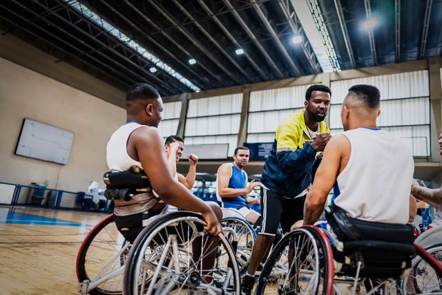 Coach handshaking wheelchair basketball player with his teammates showing support.