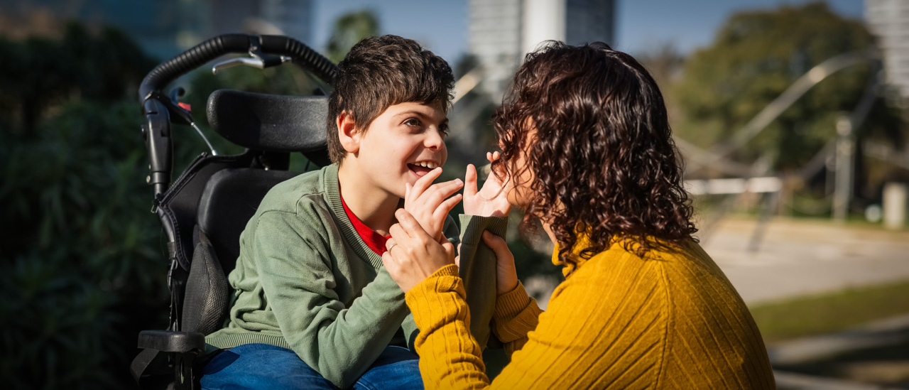 Mother interacting with her son in a wheelchair, playing together in a sunny city park.