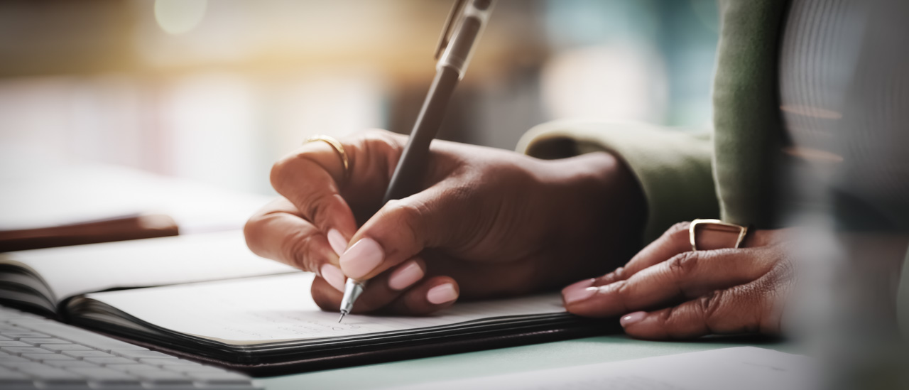 A close up of a pair of hands writing in a journal.
