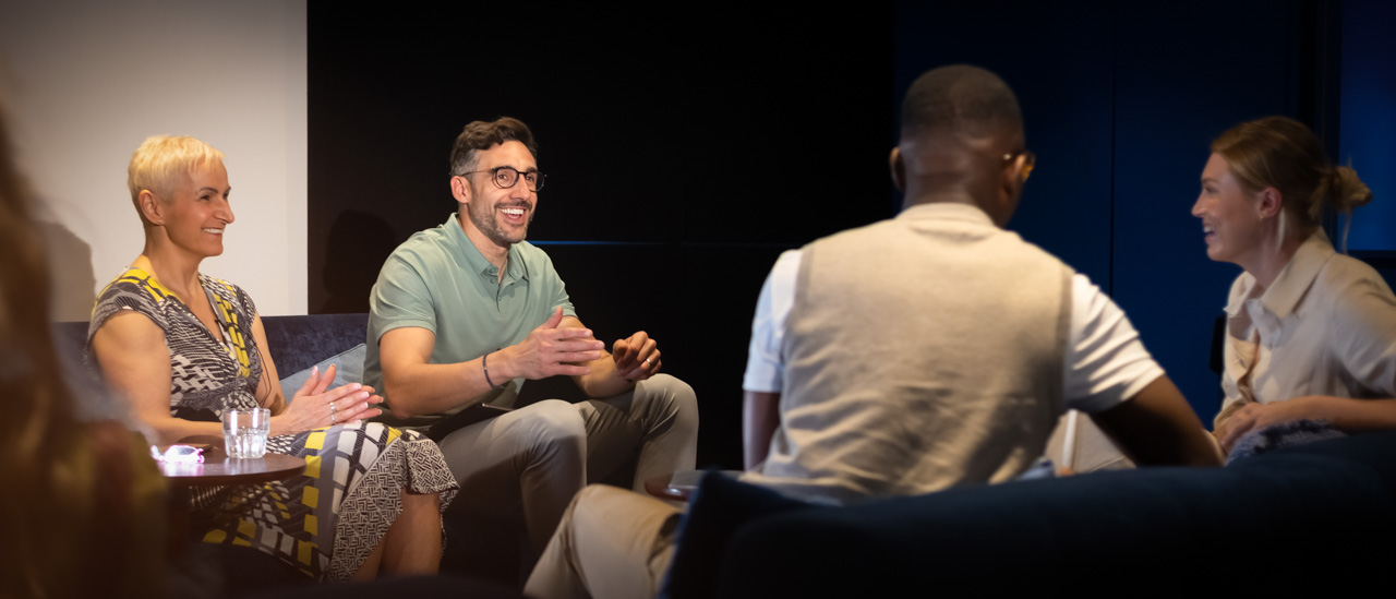 Over the shoulder shot of a group of people inside a dimly lit theatre having a captivating panel discussion.